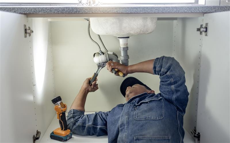 Plumber repairing pipes beneath a bathroom sink in West Chester