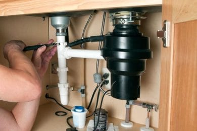 Plumber repairing a garbage disposal beneath a kitchen sink in West Chester