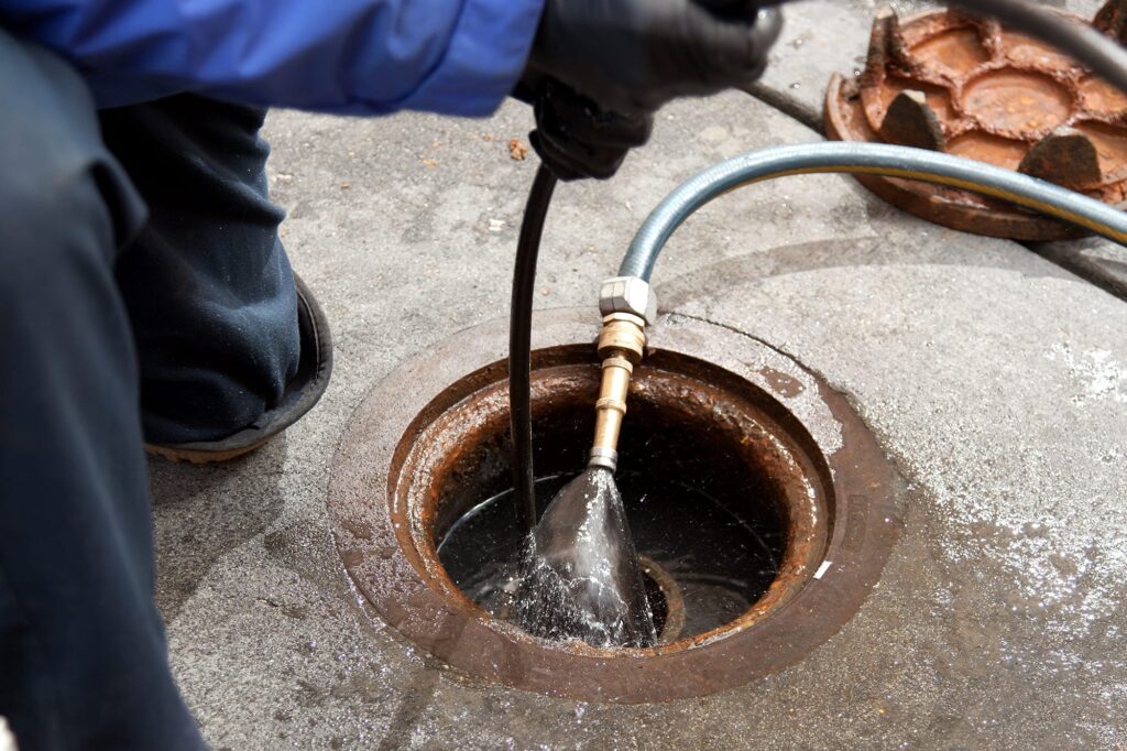 Plumber hydro jetting a sewer line through a manhole in West Chester