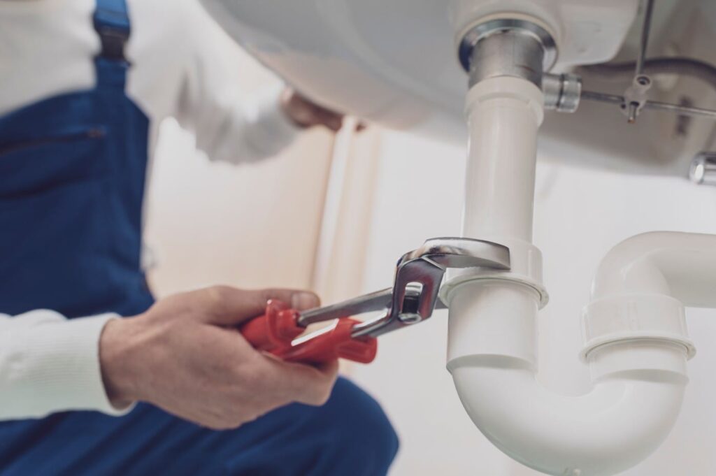 Plumber repairing a white drain pipe beneath a sink in West Chester