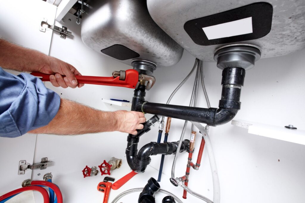 Plumber repairing drain pipes beneath a kitchen sink in West Chester